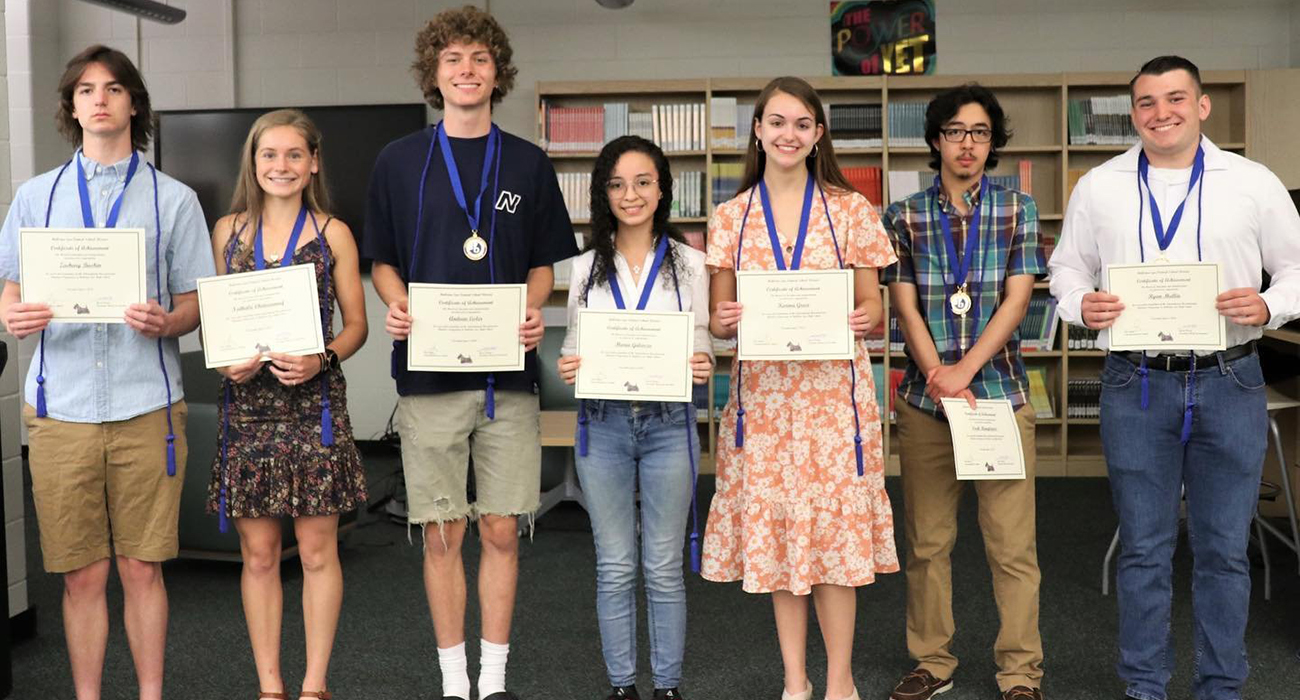 Seven teenage students standing in a line andholding up their certificates