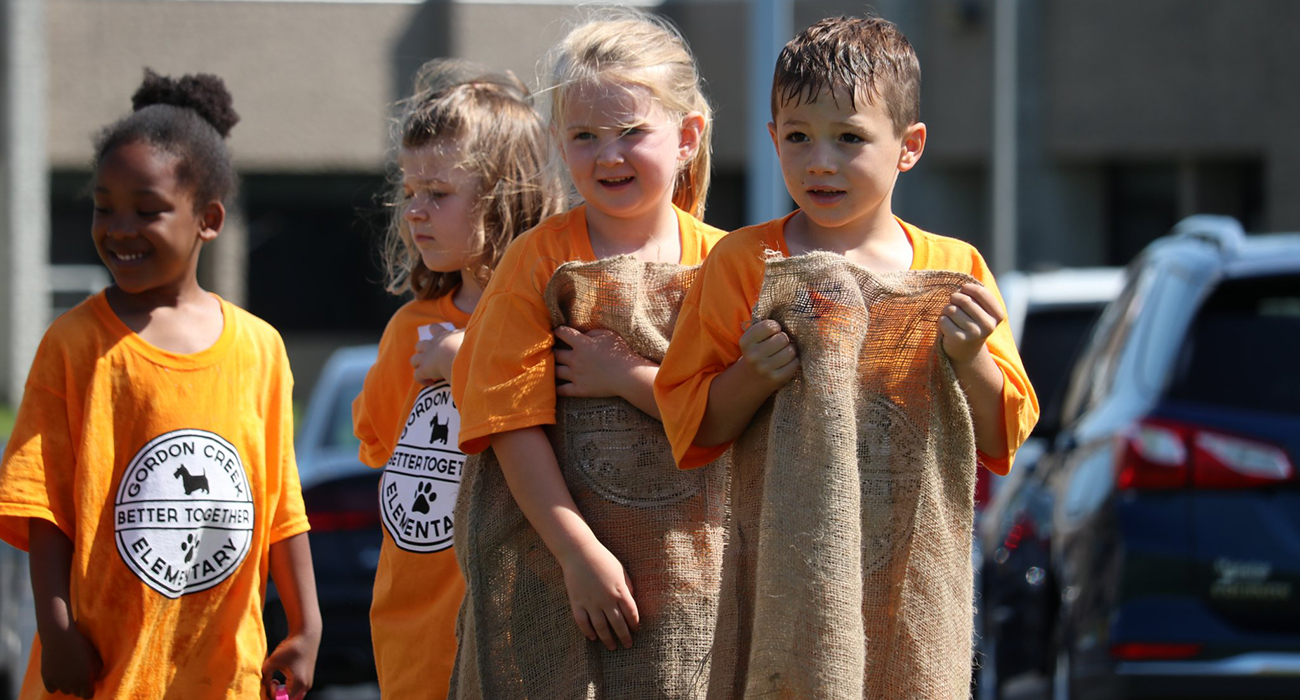 elementary students on the playground holding burlap sacks and ready to start a race in them